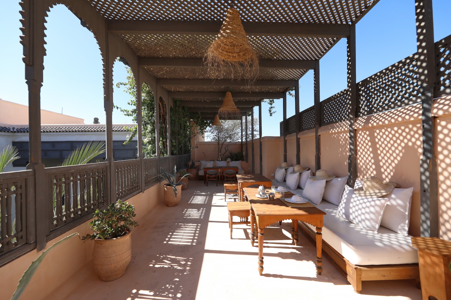 La grande pergola des toits — banquettes, coussins blancs et chapeaux de paille