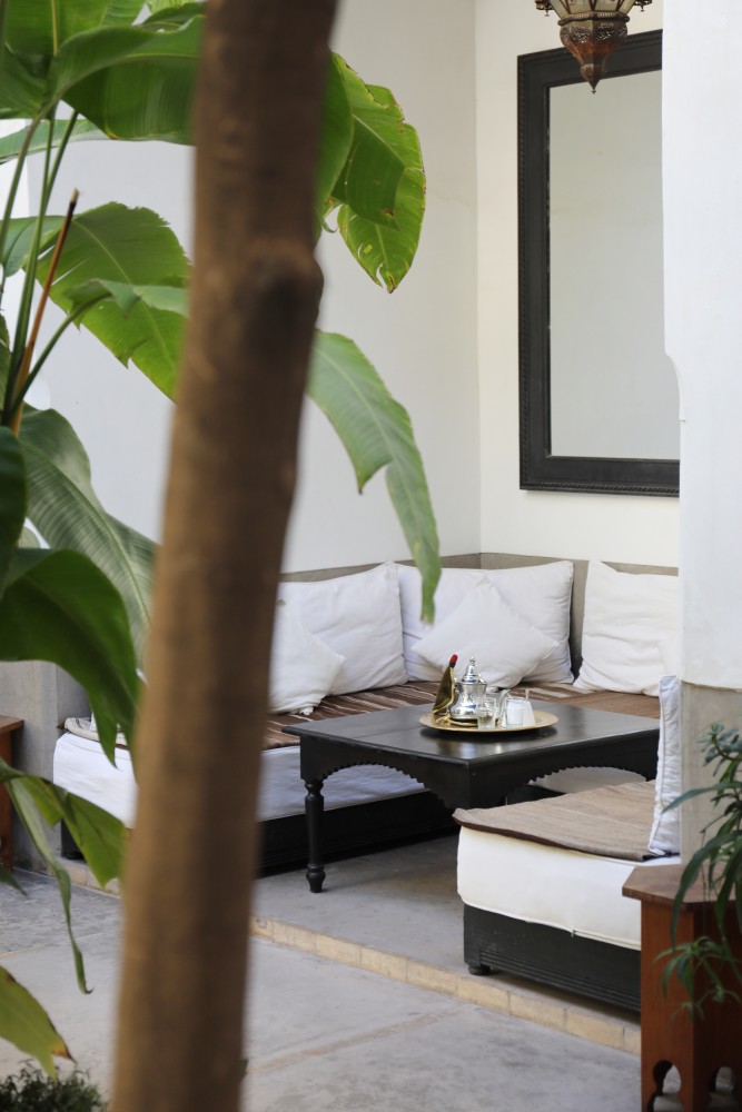 Le bhou du patio — banquettes blanches et plateau à thé, derrière les feuilles de bananier