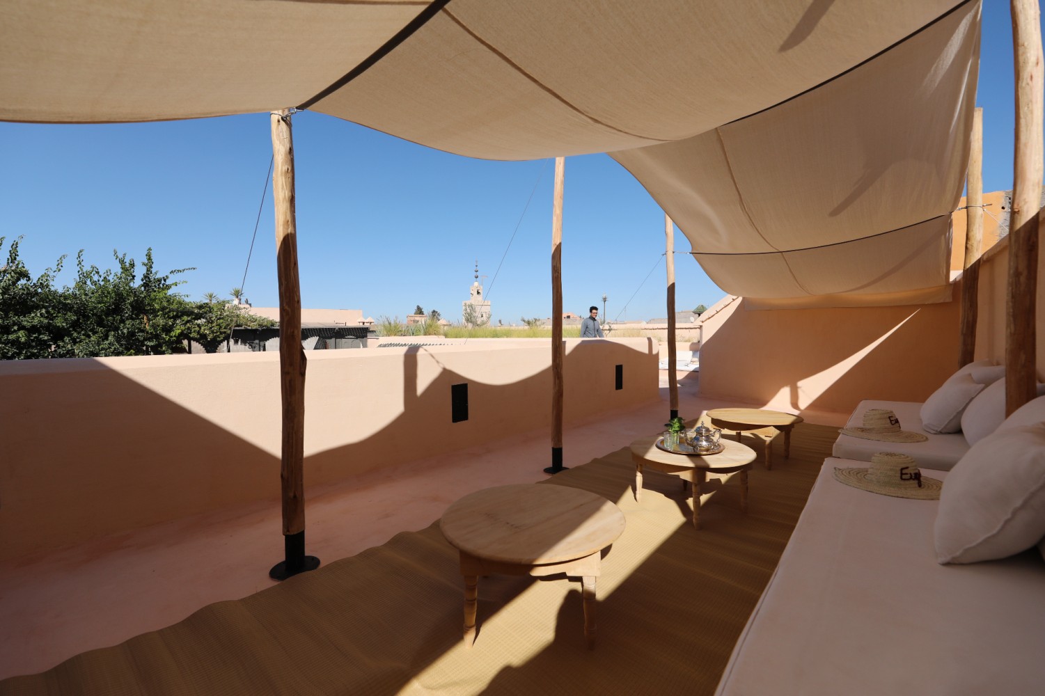 Le salon des terrasses sous les voiles d'ombrage, théière et menthe fraîche sur la table basse, minaret au loin